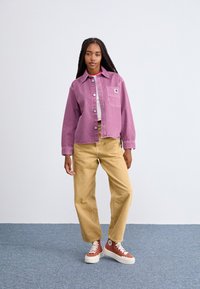 Chaqueta de mezclilla rosa, corta, con botones en la parte frontal y un bolsillo en el pecho, combinada con pantalones de pierna ancha beige y zapatillas de caña alta marrones.