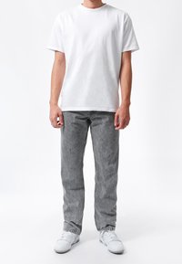 Camiseta blanca de algodón, vaqueros grises con lavado claro y zapatillas blancas. Corte recto con bolsillos laterales, sin patrones ni gráficos visibles.