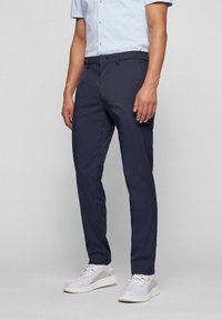 Navy trousers made of lightweight fabric, featuring a slim fit design, standard pockets, and a smooth texture. Worn with light sneakers.