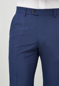 Blå skräddarsydda byxor med en slät textur, med knappstängning framtill och sidfickor, utformade för en figurnära look.