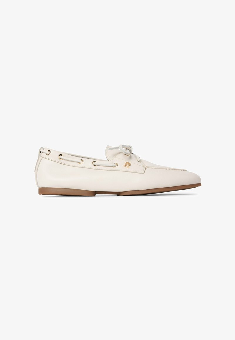White leather loafer with brown sole, lace detail around the top edge, and small gold emblem on the side.