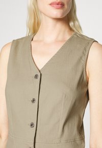 Vestido sem mangas em verde-oliva com decote em V, cinco fechos de botão e tecido texturizado. Design simples com detalhes de costura subtil.