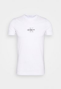 Camiseta de algodón blanca de manga corta, con cuello redondo, y un logo gris impreso "CALVIN KLEIN JEANS" en el pecho.