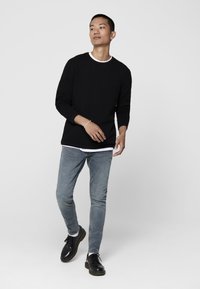 Maglione nero con texture, colletto bianco a girocollo, abbinato a jeans skinny blu chiaro e scarpe nere con lacci. Silhouette semplice e moderna.
