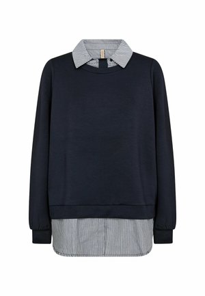 Tumši zils džemperis, pārģērbts pār melni baltu svītrainu vertikālu krekla apkakli un apakšmalu.