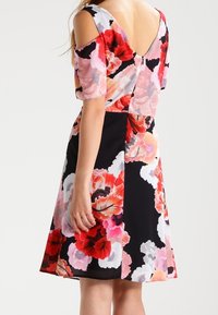 Robe à motif floral avec un corsage ajusté, des manches ouvertes sur les épaules et une jupe évasée dans des teintes de rose, rouge et noir. Tissu texturé.