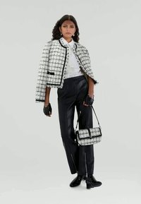 Chaqueta de tweed en blanco y negro con cuello redondo, ribete negro y bolso a juego; combinada con pantalones de cuero negros y guantes.