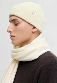 Gorro de punto acanalado en crema y bufanda a juego hechas de una tela suave. El gorro tiene una pequeña etiqueta de la marca; ambos accesorios son texturizados y acogedores.