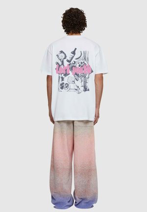 Tricou alb din bumbac cu un design grafic pe spate, având textul "tinerețe pierdută" în roz, asortat cu pantaloni largi cu un gradient pastel.