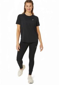 Czarna sportowa koszulka i legginsy wykonane z elastycznego materiału, z logo na piersi i gładką fakturą, w połączeniu z lekkimi trampkami.