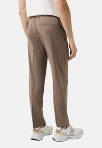 Bruine op maat gemaakte broek met een slanke pasvorm, gemaakt van gladde stof, met een enkele achterzak en gecombineerd met witte sneakers.