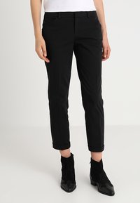 Pantalon noir slim à taille haute, avec poches avant et ourlets retroussés. Fabriqué en tissu lisse, associé à des bottines.