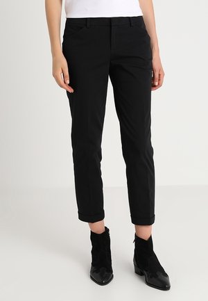 Pantalon noir slim à taille haute, avec poches avant et ourlets retroussés. Fabriqué en tissu lisse, associé à des bottines.