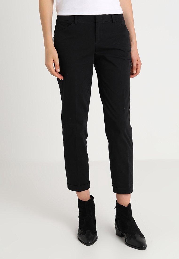 Pantalon noir slim à taille haute, avec poches avant et ourlets retroussés. Fabriqué en tissu lisse, associé à des bottines.