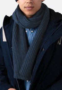 Bufanda de canalé azul oscuro hecha de tela texturizada, enrollada alrededor del cuello. Se lleva con una camisa azul y una chaqueta exterior oscura.