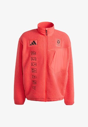 Chaqueta de forro polar en coral brillante con cuello alto, cremallera frontal y texto negro "GERMANY". Incluye parches de logotipo en el pecho y el bolsillo lateral.
