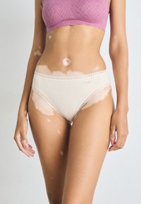 Beige high-waisted underwear with lace trim and a logo, paired with a textured light pink bralette. Smooth fabric, fitted design.