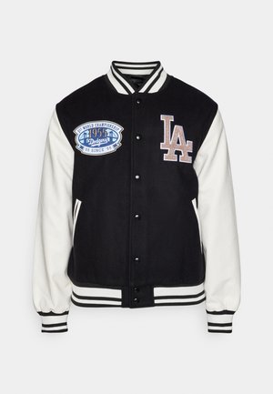 Chaqueta varsity en blanco y negro con cuerpo de lana y mangas de cuero. Presenta un parche bordado de los Dodgers y el logo "LA". Puños y dobladillo a rayas.