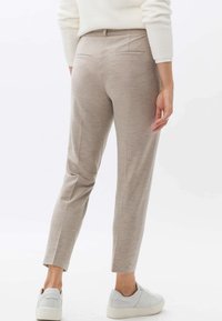 Pantalons beige ajustés avec une coupe slim, dotés de poches avant et arrière, fabriqués en tissu lisse, associés à des baskets blanches.