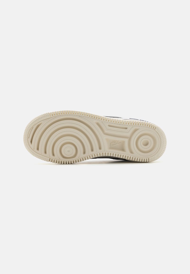 Suela blanca con patrones circulares y agarre texturizado. Presenta un logo de Nike elevado y una superficie lisa. Principalmente beige con un ligero contraste.