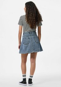 Jupe en denim à coupe évasée, avec deux poches arrière et un ourlet effiloché. Associée à une chemise rayée noir et blanc et à des baskets noires avec des semelles blanches.