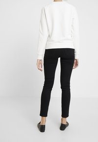 Witte trui met geribbelde manchetten en zoom, gecombineerd met zwarte skinny jeans en zwarte instapschoenen, gezien van achteren.