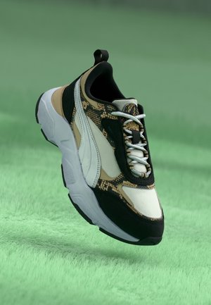 Sneakers med sorte, beige og hvide paneler, slangeprint accenter, grå snørebånd og en tyk hvid sål på en grøn tekstureret overflade.
