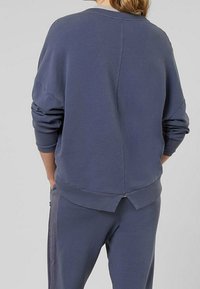 Modrá mikina oversized střihu s klesajícími rameny, texturovanou látkou a rozparkem na zadním lemu. Žebrované manžety a lem přidávají jemné detaily.