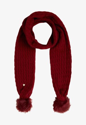 Écharpe tricotée rouge foncé avec motif torsadé, pompons en fausse fourrure aux deux extrémités, et une petite étiquette métallique en forme de cœur sur un côté.