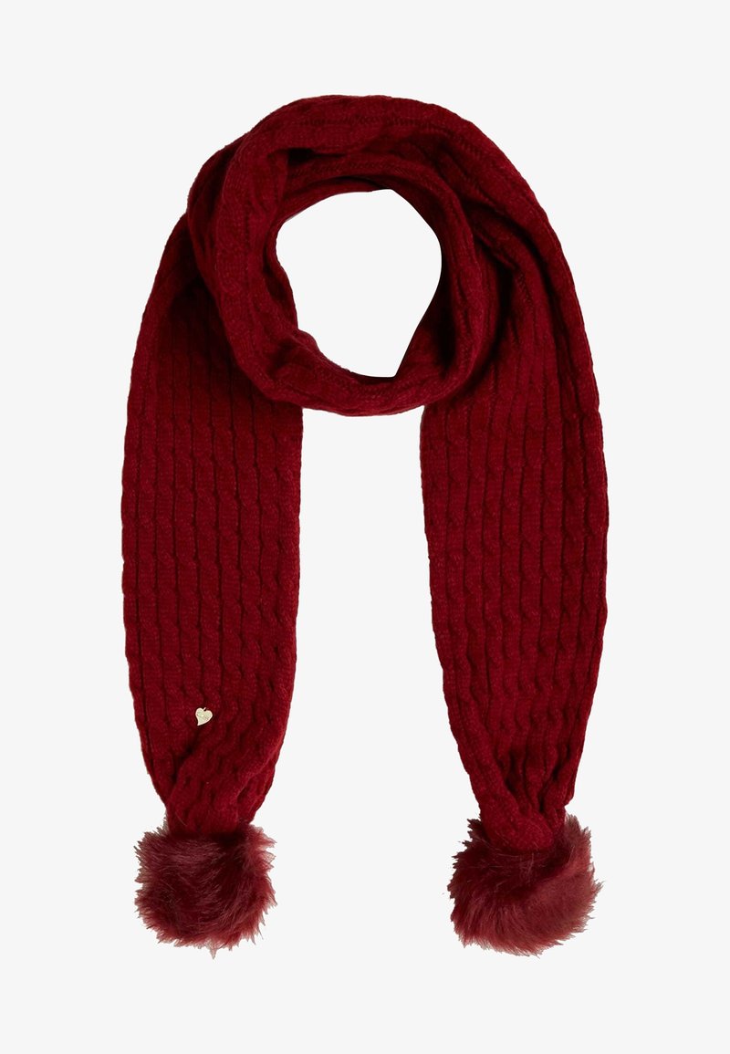 Écharpe tricotée rouge foncé avec motif torsadé, pompons en fausse fourrure aux deux extrémités, et une petite étiquette métallique en forme de cœur sur un côté.