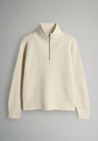 Kermanvärinen neulepaita, jossa on korkea kaulus ja puolivetoketju. Paidassa on teksturoitu ribbikuvio ja leveät hihat, jotka on suunniteltu mukavuutta silmällä pitäen.