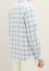 Chemise à carreaux bleu clair et blanc avec manches longues, détails à boutons sur les poignets et coupe décontractée. Tissu doux avec un motif à carreaux.