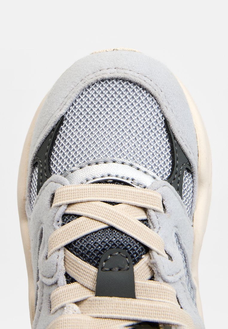 Jasnoszare sneakersy z siateczkową cholewką, zamszowymi akcentami, beżowymi sznurowadłami i czarnymi detalami. Okrągły czubek i teksturowana powierzchnia.