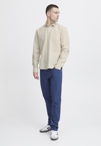 Bežna majica s long sleeves in sprednjim žepom, kombinirana s temno modrimi hlačami in belimi supergami z črnimi detajli. Preprost, prilagojen kroj.