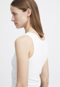 Weißes geripptes Tanktop mit breiten Trägern, figurbetonter Passform, weichem Material und rundem Ausschnitt, seitlich gezeigt.