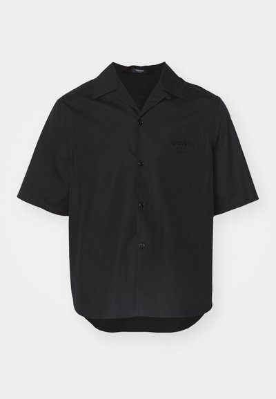 Chemise noire à manches courtes en tissu lisse, avec un col pointu, des boutons à l'avant et une poche poitrine avec un logo en relief.