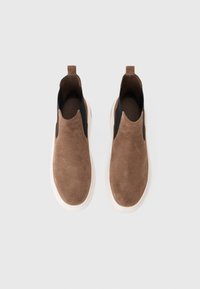 Barna velúr slip-on cipők fekete elasztikus oldalsó panelekkel és fehér gumitalppal. Minimalista dizájn, amelynek hátulján kis húzófül található.