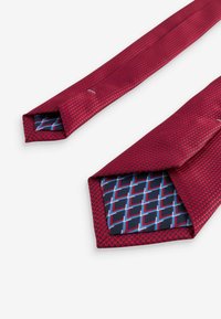 Red patterned tie with a textured surface. The underside features a geometric blue and black design. Tapered ends.