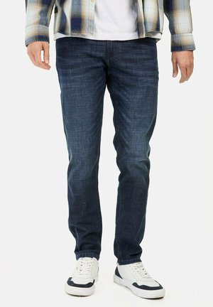 Dunkelblaue Jeans aus Denim im Slim-Fit, mit glatter Textur, klassischen Taschen und einem ausgewaschenen Finish, kombiniert mit weißen Sneakern.