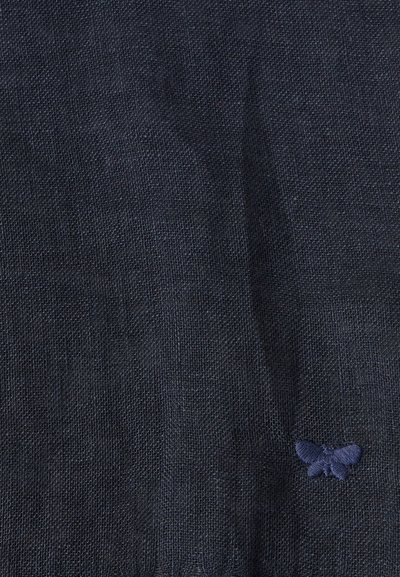 Tissu bleu marine foncé avec une texture tissée subtile, présentant un petit papillon brodé dans le coin inférieur droit.