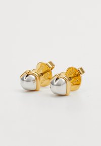 Guld- och silverörhängen i rundad form, med en glänsande yta och präglad logotyp på baksidan.