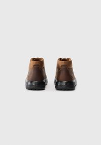 Ruskea nahkainen nilkkaboots, jossa on vaaleanruskea kangasreuna ja kestävä musta kumipohja. Minimalistinen muotoilu, jossa on teksturoitu pinta.