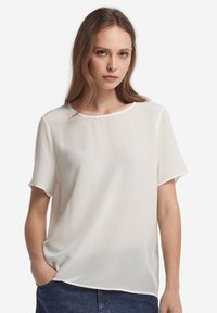 Vit kortärmad blus i lätt, slät kvalitet med rund halsringning och avslappnad passform, med en enkel, minimalistisk design.