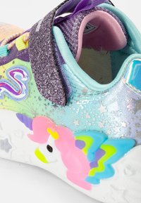 Dětské tenisky v několika barvách s třpytivým fialovým páskem, duhovými detaily a vyvýšeným designem jednorožce na patě.