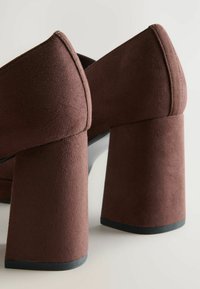 Pantofi cu toc înalt din suede maro, cu tocuri pătrate late, având un design elegant cu vârf ascuțit și un finisaj texturat.