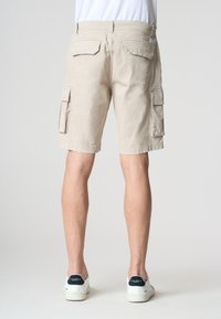 Pantaloni cargo beige con più tasche laterali, tasche posteriori piatte e una vestibilità comoda, abbinati a sneaker bianche con dettagli scuri.