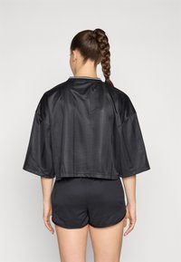 Černá saténová zkrácená bunda s širokými rukávy, se pruhovanou texturou a černobílým límcem, zkombinovaná s černými šortkami.