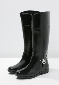 Czarne kalosze do kolan wykonane z błyszczącego materiału. Posiadają srebrny akcent logo oraz detale z klamrą po boku. Płaska podeszwa.