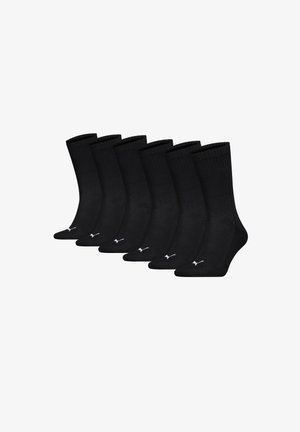 Sept chaussettes noires de type crew avec logos Puma blancs sur les orteils, disposées côte à côte sur un fond blanc.