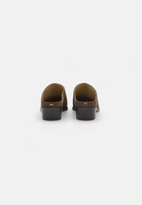 Brune semskede mules med en lav sort hæl, med en afrundet tå og åben bagdesign, ideelle til nemt at tage på.